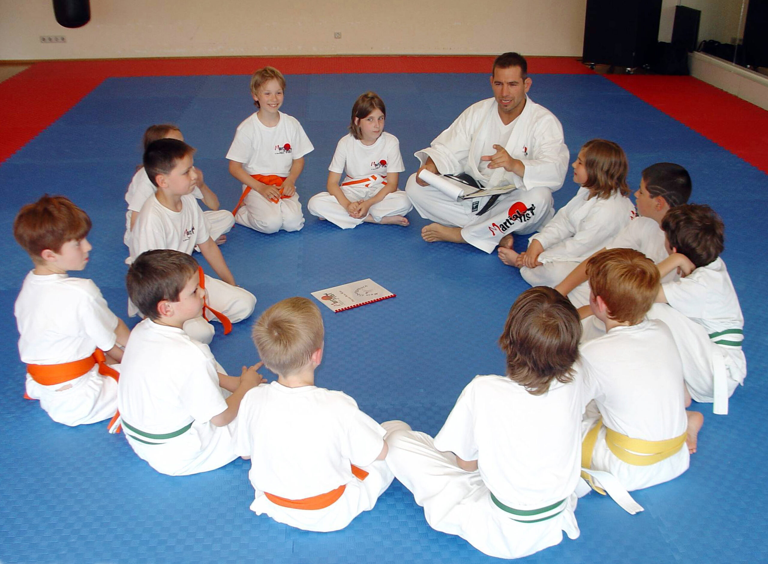 Eine Gruppe Kinder sitzt in einem Kreis und achtet auf Carsten Ziegler, der etwas erklärt